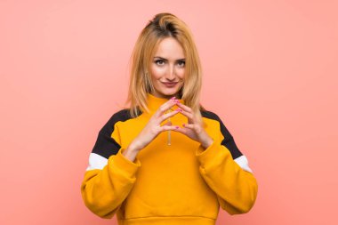 Soyutlanmış pembe arka plan entrikaları kuran genç sarışın kadın.