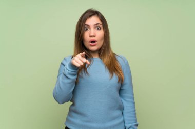 Young girl over green wall surprised and pointing front