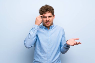 Sarışın adam mavi duvar parmak kafasına koyarak delilik jest yapma