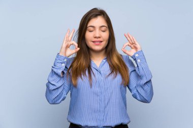 Young girl over isolated blue wall in zen pose