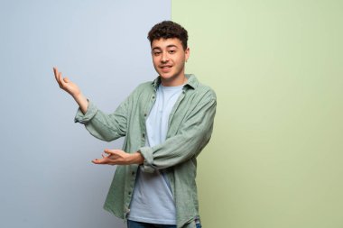 Mavi ve yeşil arka plandaki genç adam davetli olduğu için ellerini yana uzatıyor.