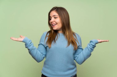 Young girl over green wall holding copyspace with two hands