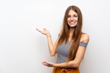 İzole edilmiş beyaz duvarın üzerinde uzun saçlı genç bir kadın. Gelmesi için ellerini yana uzatıyor.