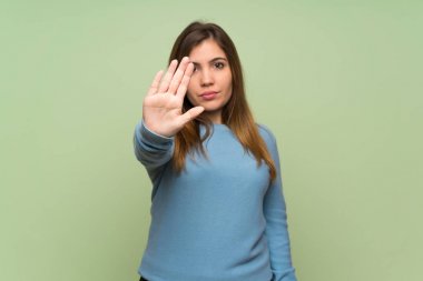 Young girl over green wall making stop gesture