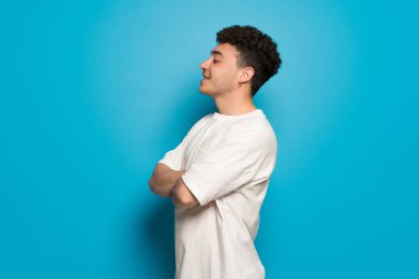 Mavi arka plandaki genç adam yan pozisyonda.