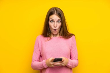 Izole sarı duvar üzerinde uzun saçlı genç kadın şaşırttı ve bir mesaj gönderme