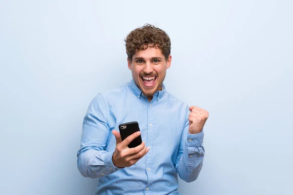 Blonder Mann Über Blaue Wand Mit Handy Siegerpose — Stockfoto