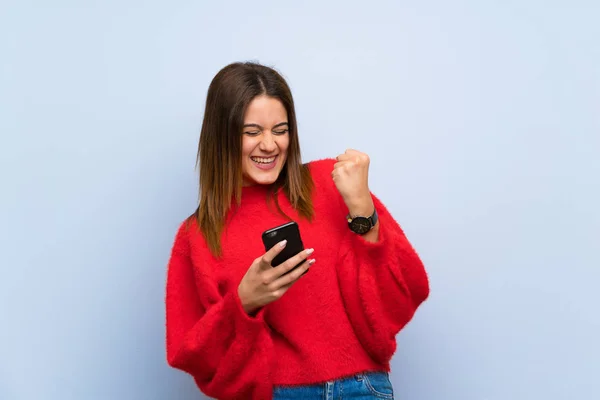 Jonge Vrouw Geïsoleerde Blauwe Muur Met Telefoon Overwinnings Positie — Stockfoto