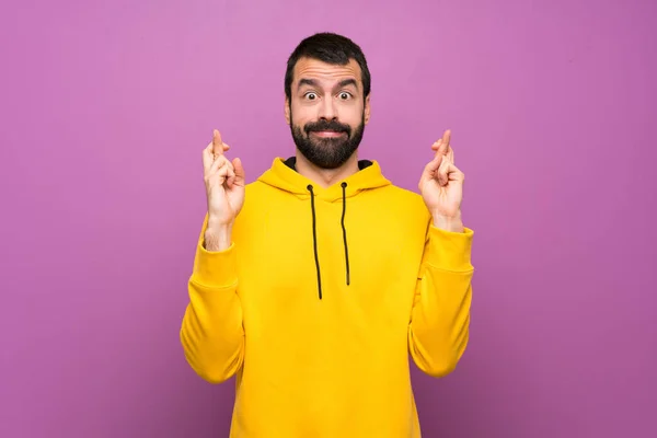 Handsome man with yellow sweatshirt with fingers crossing and wishing the best