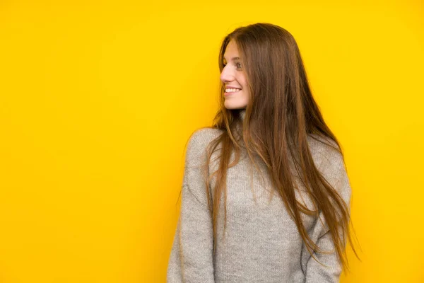 Young woman with long hair over yellow background standing and looking to the side