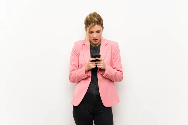 Young blonde woman with pink suit surprised and sending a message
