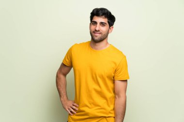 Genç adam pembe duvarın üzerinde kolları kalçasında ve gülümsüyor.