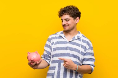 Sarı duvar üzerinde bir kumbara tutan sarışın adam