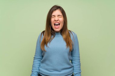 Young girl over green wall shouting to the front with mouth wide open