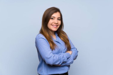 Young girl over isolated blue wall with arms crossed and looking forward