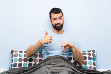 Yatakta iyi-kötü işareti yapan bir adam. Evet ya da değil arasında kararsız