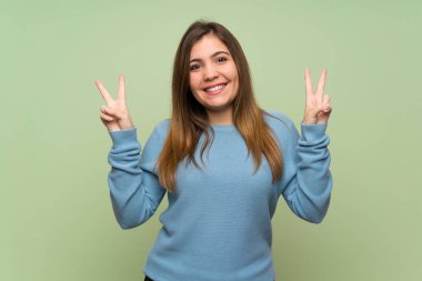 Young girl over green wall showing victory sign with both hands