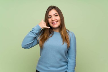 Young girl over green wall making phone gesture. Call me back sign