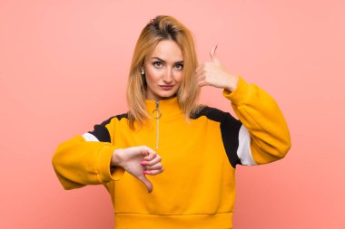 Soyutlanmış pembe arka planı olan genç sarışın kadın iyiye-kötüye işaret yapıyor. Evet ya da hayır arasında kararsız