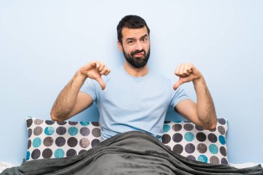 Yatakta başparmağını aşağı gösteren adam