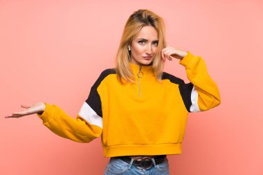 Soyutlanmış pembe arka planı olan genç sarışın kadın deliliğin jestini yapıyor. Parmağını kafaya koyuyor.