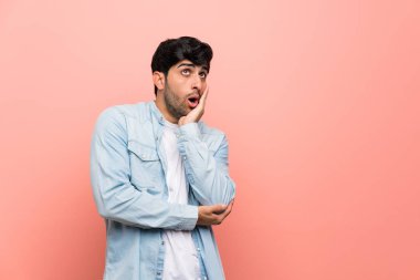 Pembe duvar üzerinde genç adam sürpriz ve doğru bakarken şok