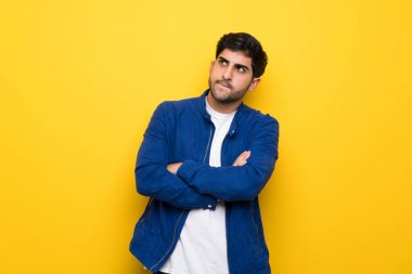 Sarı duvar üzerinde mavi ceketli ve yüz ifadesi karıştıran adam