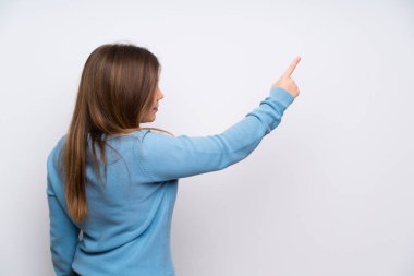 Young girl with blue sweater pointing back with the index finger