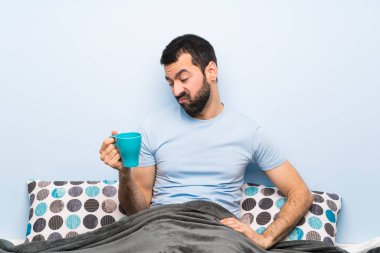 Bir fincan kahve tutan sakallı adam yatakta