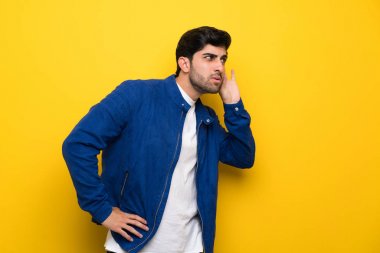 Adam bir şey kulak el koyarak dinleme sarı duvarın üzerinden mavi ceket ile