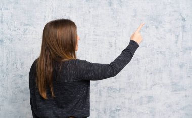 Young girl over grunge wall pointing back with the index finger