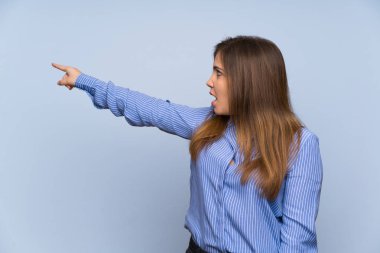 Young girl over isolated blue wall pointing away