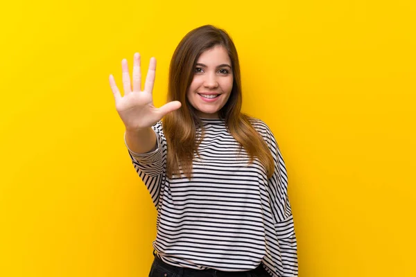 Młoda Dziewczyna Nad Żółtą Ścianą Licząc Pięć Palcami — Zdjęcie stockowe