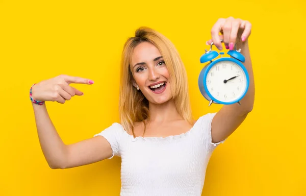 Mujer Rubia Joven Sobre Pared Amarilla Aislada Sosteniendo Reloj Despertador —  Fotos de Stock