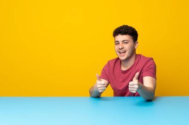 Önünü gösteren renkli duvarlı ve masalı genç adam gülümsüyor.