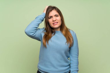 Young girl over green wall with an expression of frustration and not understanding