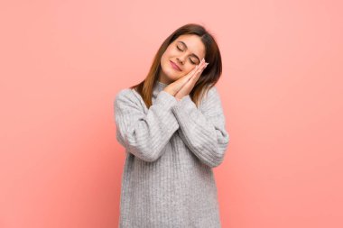 Pembe duvarın ardında genç bir kadın uyku jesti yapıyor.