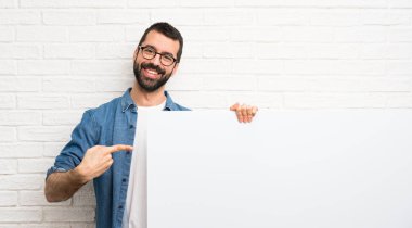 Boş bir pankart tutan beyaz tuğla duvar üzerinde sakallı yakışıklı adam