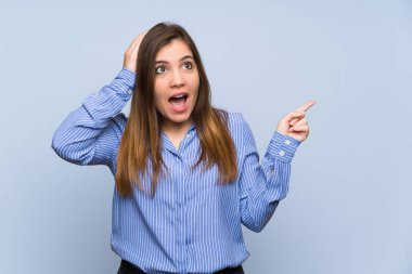 Young girl over isolated blue wall surprised and pointing finger to the side