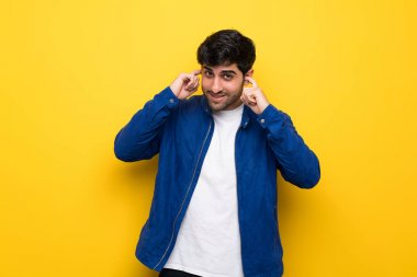 Sarı duvar üzerinde mavi ceketli adam sinirli ve kulakları kapsayan