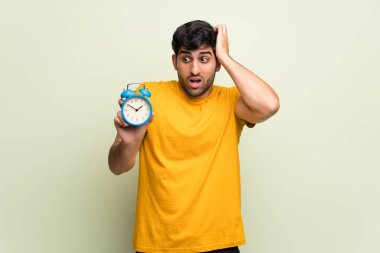 Pembe duvarın üzerinde genç bir adam huzursuz çünkü geç oldu ve elinde klasik çalar saat var.