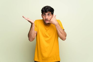 Pembe duvarın üzerindeki genç adam şaşırdı ve telefon jesti yaptı.