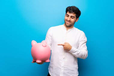 Genç adam bir servet tutan izole mavi duvarın üzerinden