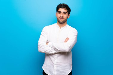 Genç adam mavi duvarı aştı. Kollarını ön cephede çapraz tutuyor.