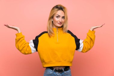 Soyutlanmış pembe arka planda genç sarışın kadın şüpheli hareketler yapıyor.