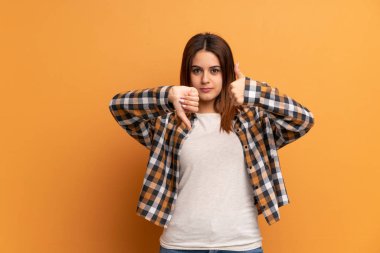 Kahverengi duvarın arkasındaki genç kadın iyiye-kötüye işaret veriyor. Evet ya da hayır arasında kararsız