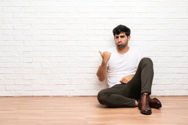 Genç adam yerde mutsuz bir şekilde oturuyor ve onu işaret ediyor.
