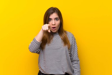 Young girl over yellow wall surprised and pointing front