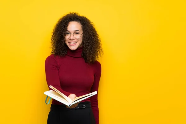 Dominican woman with turtleneck sweater holding a book and giving it to someone