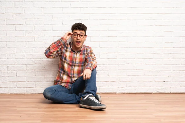 Junger Mann Sitzt Mit Brille Auf Dem Boden Und Überrascht — Stockfoto